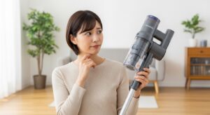 自宅のフローリングでツインバードのスティック掃除機を手に、その評判について思案する日本人女性。